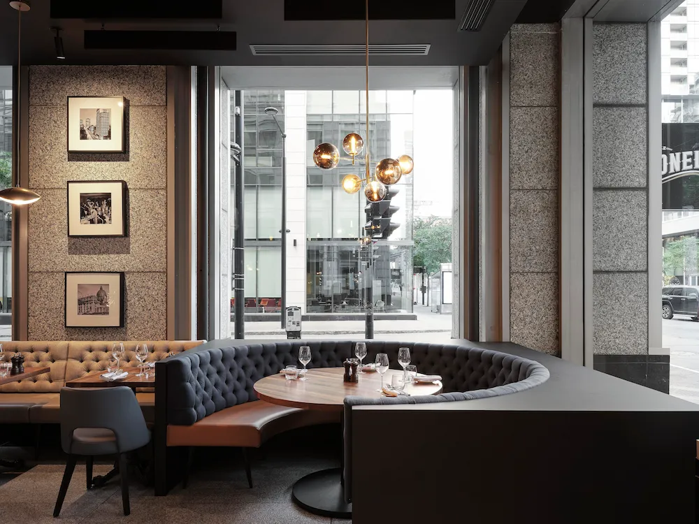 Modern Restaurant Interior with a Circular Tufted Booth Around a Round Table Set with Wine Glasses, by Large Windows.